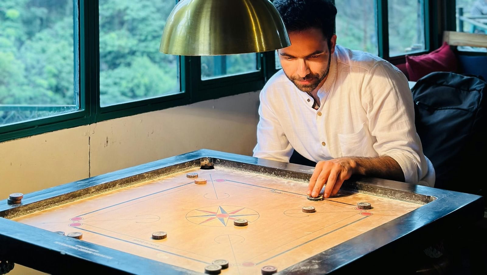 A man playing carrom on a wooden carrom board indoors.