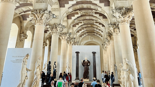 An ornate hall with tall columns and a vaulted ceiling featuring geometric patterns.