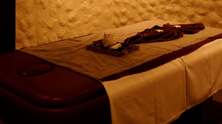 A serene spa treatment room with a massage bed, textured white walls, and soft, golden ambient lighting at Hotel Hukam's Lalit Mahal.