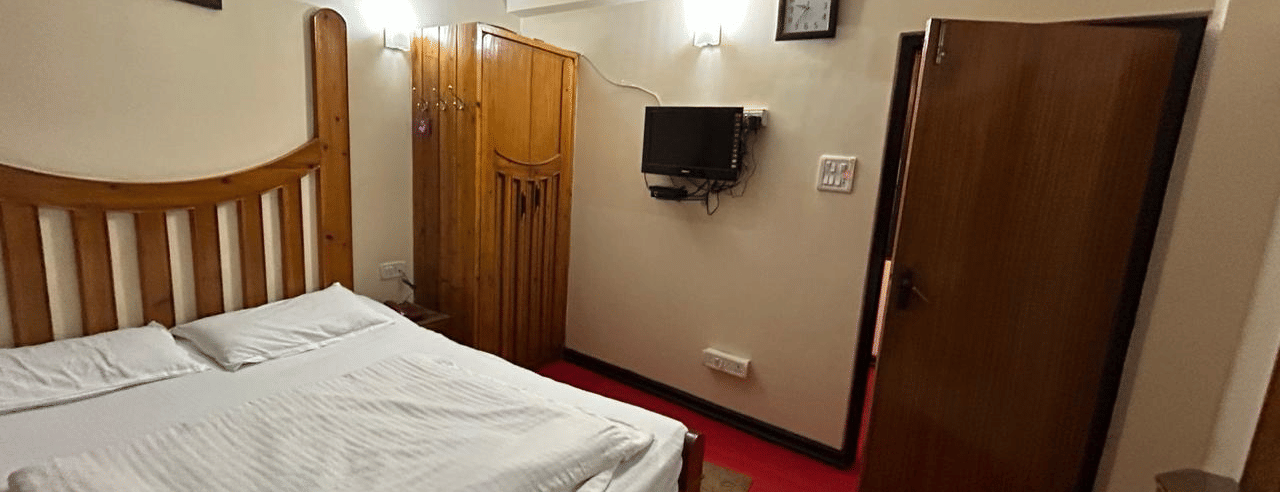 Room with a double bed, wooden furniture, a wardrobe, and a television mounted on the wall at Hotel Dolphin Darjeeling.