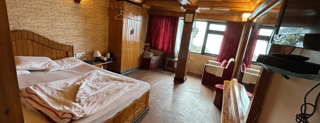 Spacious room with a double bed, red and wood decor, a mirror, and a view through a balcony door at Hotel Dolphin Darjeeling.
