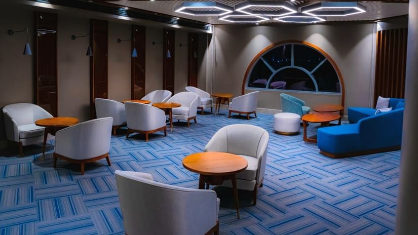 A wide angle shot of our restaurant in Hargeisa featuring round wooden tables, cushioned chairs, and bright ceiling fixtures - Serene Sarovar Premiere Hargeisa