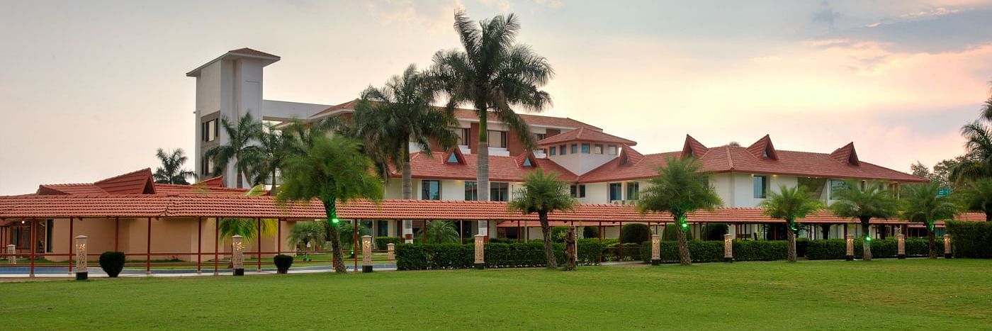 Exterior view showcasing lush grass and palm trees encircling the resort under a partly cloudy sky  | Crescent Spa & Resorts