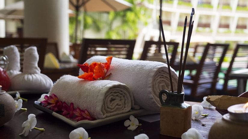 Two rolled up towels placed on a tray decorated with flowers, and an incense stand placed on a table with the background of The Bristol Hotel offering corporate outing in Gurgaon.