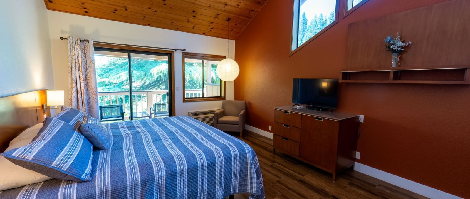 A Deluxe King Room at Amador Hotel with a wooden ceiling, a king-sized bed with striped bedding, and a TV on a dresser.