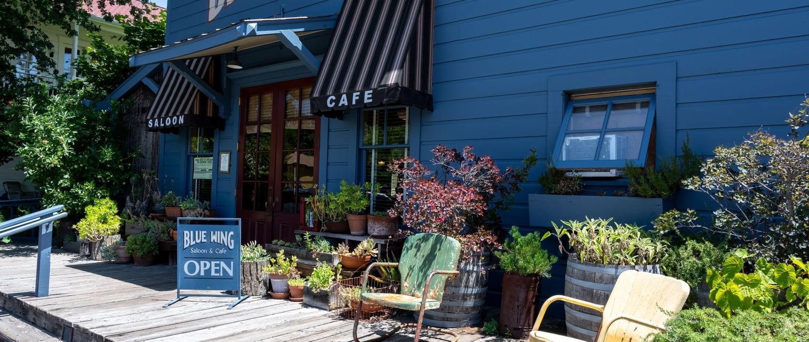 The charming exterior of the Blue Wing restaurant with outdoor seating and lush greenery at The Tallman Hotel.