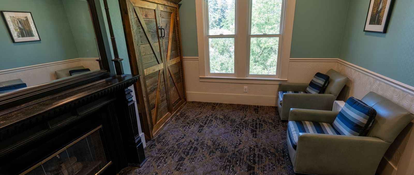 Spacious sitting area with armchairs and a fireplace beside tall windows at The Groveland Hotel.