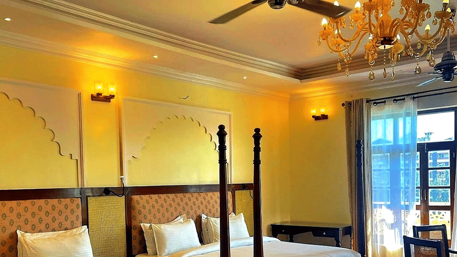 A room with a twin large bed, spreads, pillows, a fan, chairs, and a chandelier. | Hotel Devnadi, Haridwar