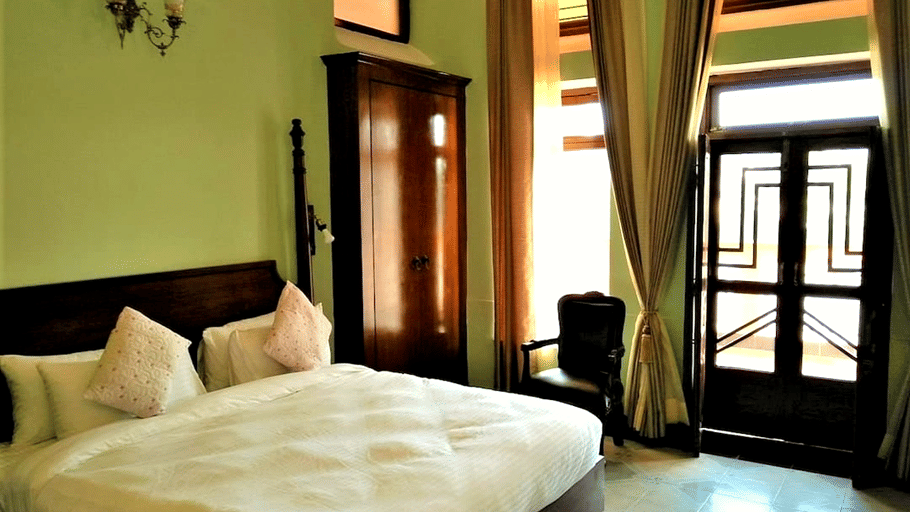 A room with a large bed, spreads, pillows, and windows. | Hotel Devnadi, Haridwar
