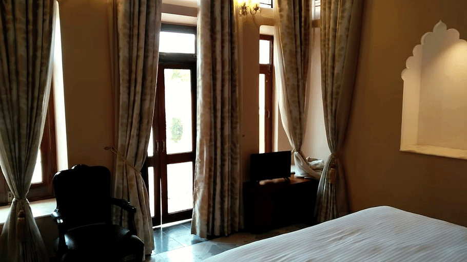 A room with a large bed, spreads, pillows, and windows. | Hotel Devnadi, Haridwar