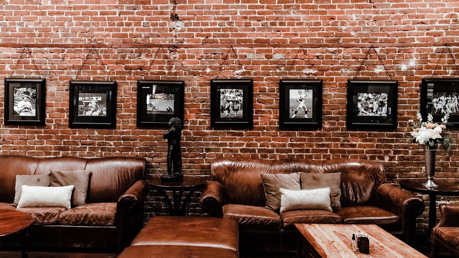 Sitting arena with brown sofas and wooden tables accompanied by brick textured wall with hanging wall art in the background 