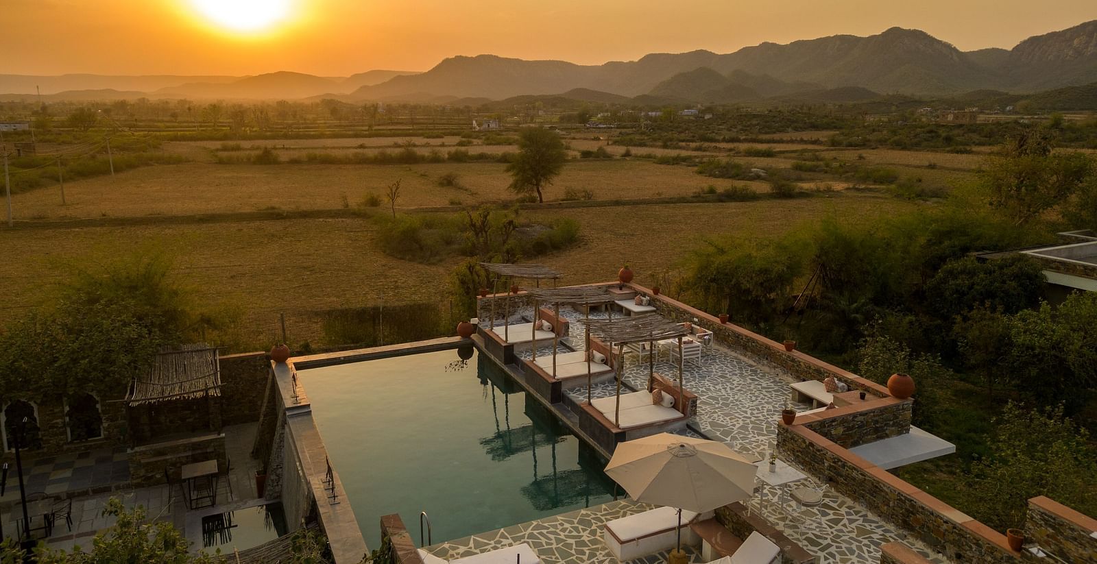 A serene sunset seen in the shot with a roof top swimming poll below it - Utsav Camp
