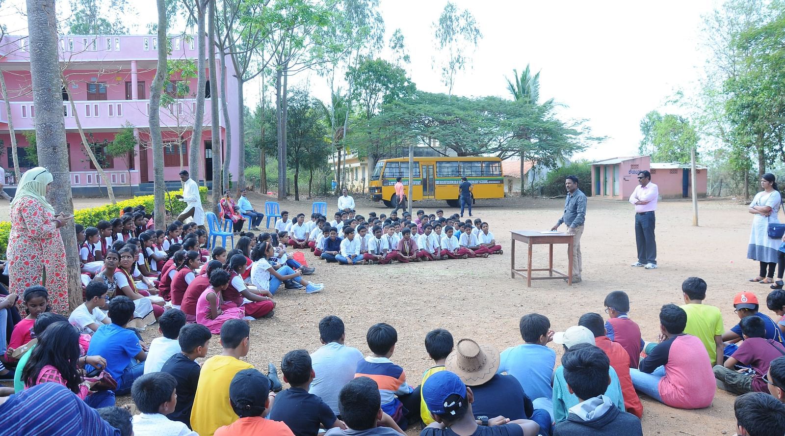 image of people sitting on the ground and a person adressing them from the middle in a government school