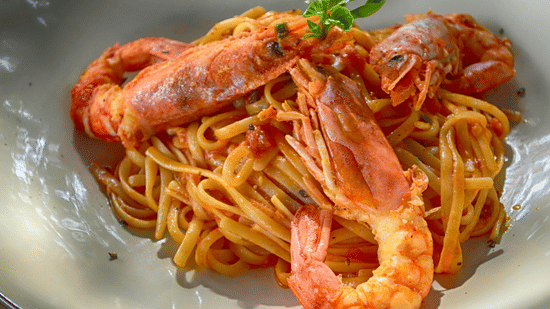 Prawns and pasta in a rich red sauce are served together in a white bowl.