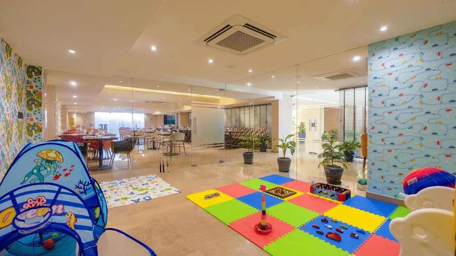 A wide-angle shot of the indoor kids' play area at Hotel 91 Privé, Gurugram, with a colourful mat and a kids slide.