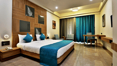 Double bed with blue pillows and bed runner with a wall mounted tv opposite it inside Deluxe Room at VITS Devbhumi, Dwarka