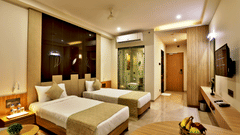 twin beds with gold pillows and bed runner with a wall mounted tv opposite it inside Executive Room - VITS Devbhumi, Dwarka