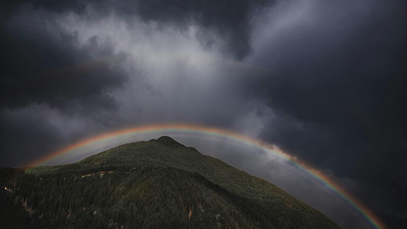 Dramatic sky over a hilltop with a vibrant rainbow arching through dark clouds.
