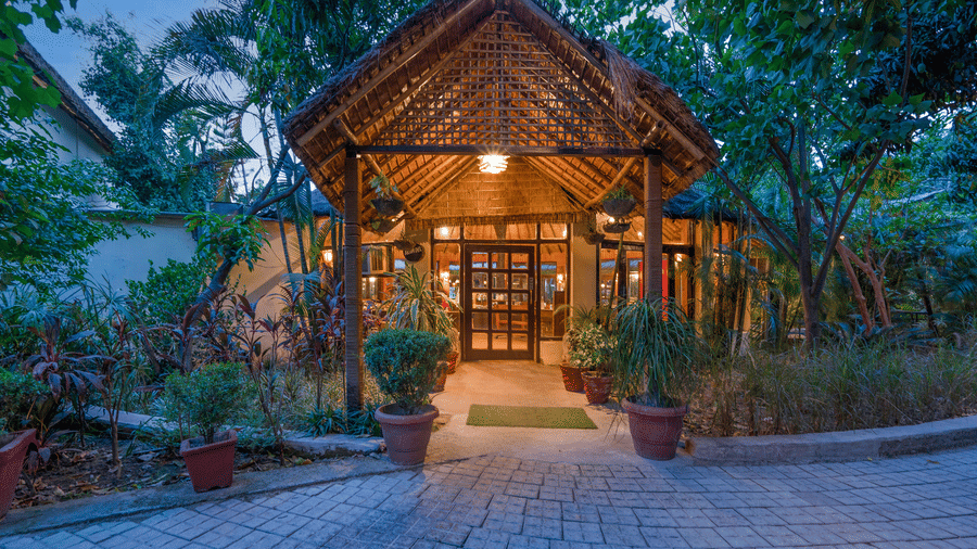 An exterior view of the resort villa nestled behind tropical palm trees and dense green foliage under a clear blue sky.