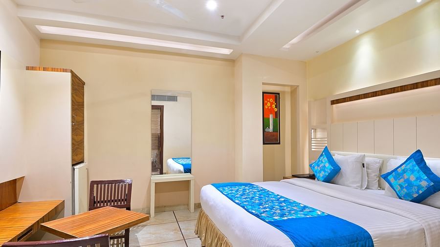 Super Deluxe Room at Hotel Hari Piorko featuring a plush ed with fresh linen and blue bed runner along with cushions and its reflection partially visible on the mirror next to it on the wall