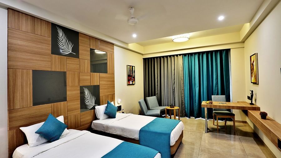 A twin bed with blue pillow and bed runners on it and a study table in the background inside the Deluxe Room - VITS Devbhumi, Dwarka