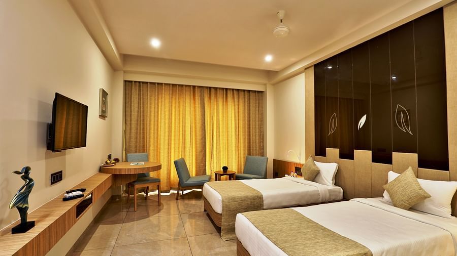 twin beds with gold pillows and bed runner with a wall mounted tv opposite it inside Executive Room - VITS Devbhumi, Dwarka