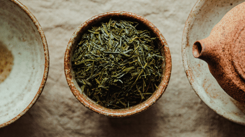 A view from above of a cup filled with tea leaves with a tea pot next to it.