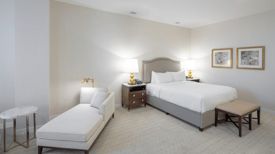 A well-lit Lakeview King Room at YO1 Longevity & Health Resorts featuring a sitting space and a side table by a plush bed with a lamp on the nightstand