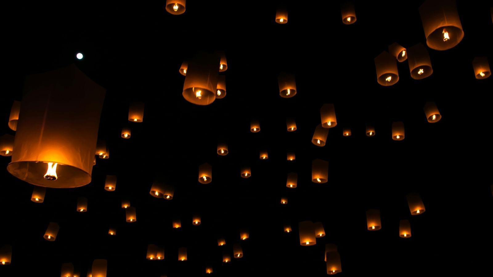 Dozens of glowing sky lanterns floating upwards in the dark night sky.