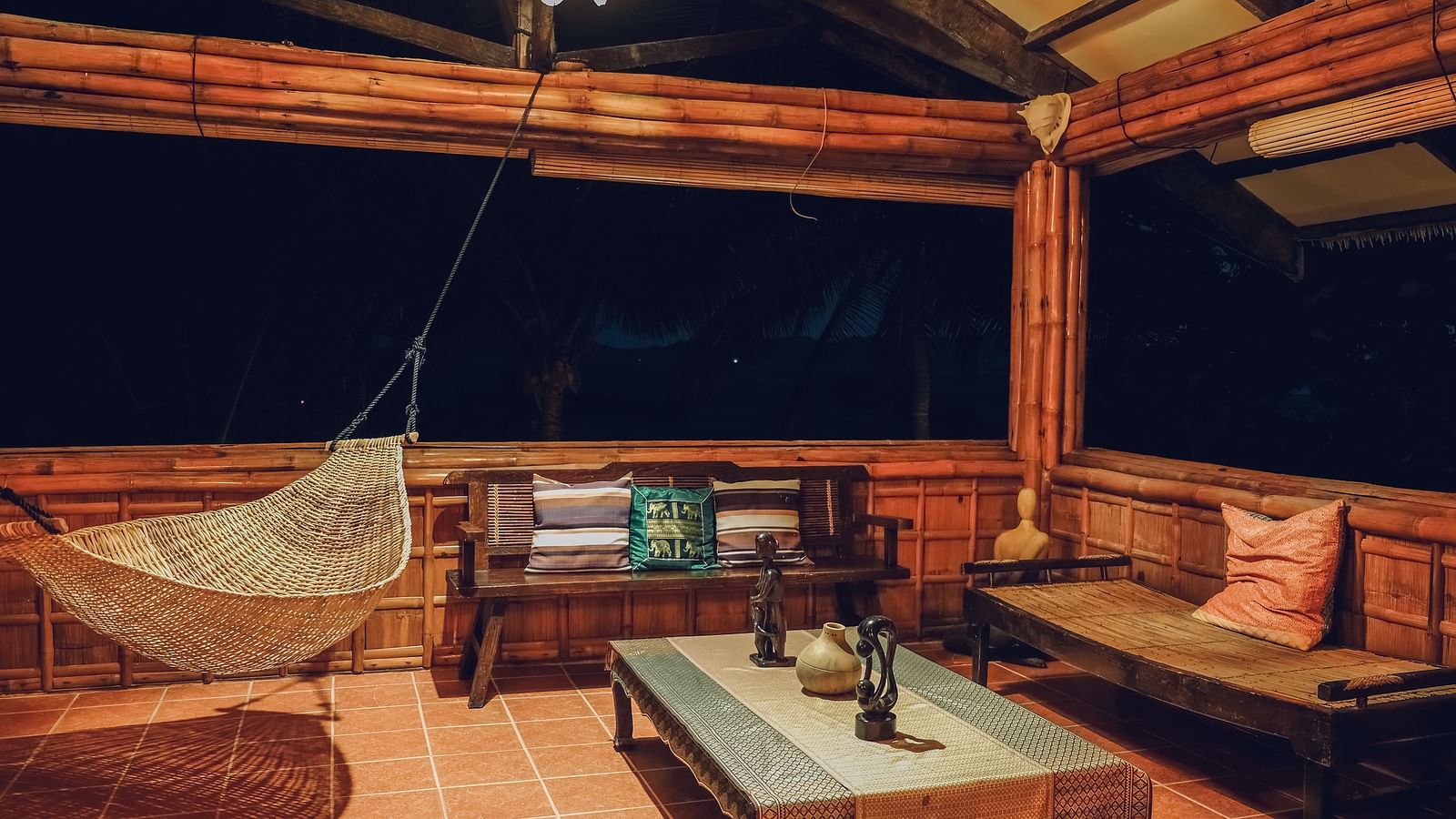 Sitting area at Flower Island Resort featuring a cosy setting with wooden seating area, a hammock, and warm lighting.