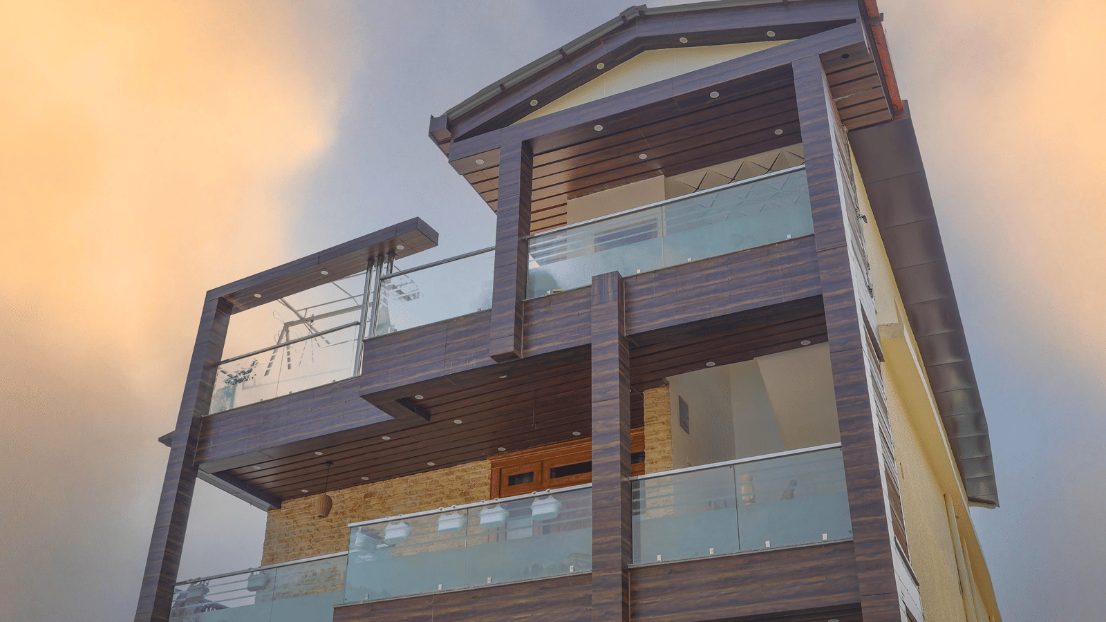 The facade of Perfectstayz Value Paradise, Mussoorie with glass balconies and wooden exterior under a cloudy sky.