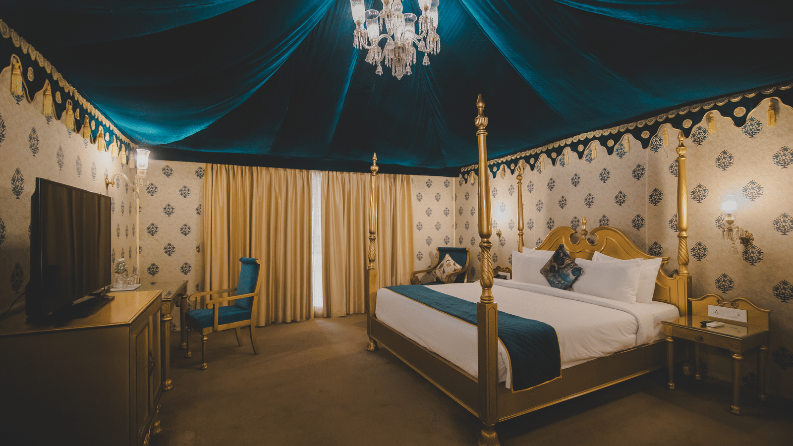 A room with a bed and a television in front inside royal luxury tent with balcony at Rajasthali Resort & Spa Jaipur.