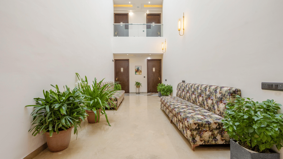 An empty corridor at Hotel 91 Privé, Gurugram, with a seating area along with several potted plants.