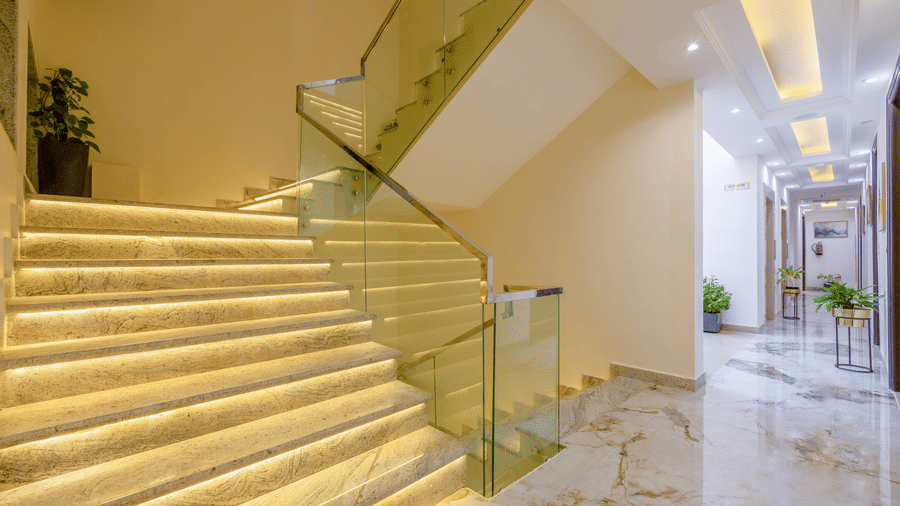 A beautiful stairway with the staircase brightly glowing with golden lights with a glass railing at Hotel 91 Privé, Gurugram.