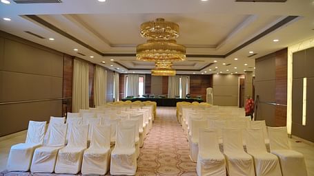 Banquet hall with rows of white chairs arranged in theatre style, lit by a chandelier above at Rang Lords Inn Bharuch