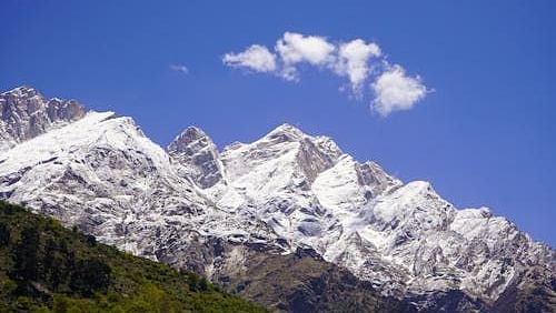 Snow-capped Himalayan peaks under a deep blue sky, with a patch of green hillside and a single cloud floating above.