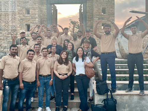 Aramness Gir staff standing together outdoors on a stone pathway near old stone walls, posing and cheering toward the camera.