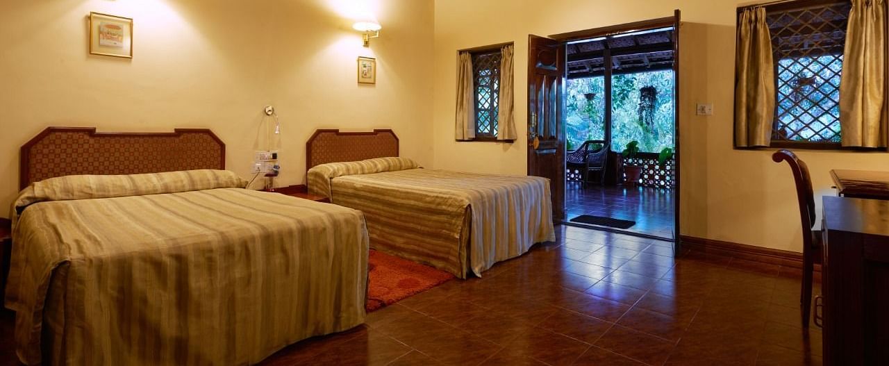 Spacious room with twin beds, wooden ceiling beams, and windows showing greenery - BluSalzz Collection - Tranquil Resort, Wayanad