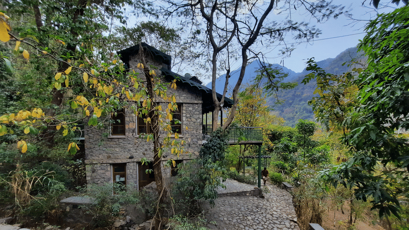Facade view of Neemrana's Glasshouse on The Ganges amidst the nature with mountains and clear blue sky in the background.
