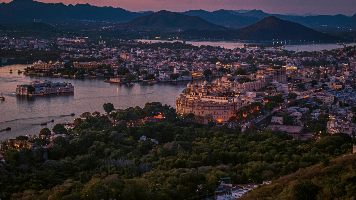 Aerial night view of Udaipur city with illuminated buildings, lakes, and surrounding hills under a dark sky