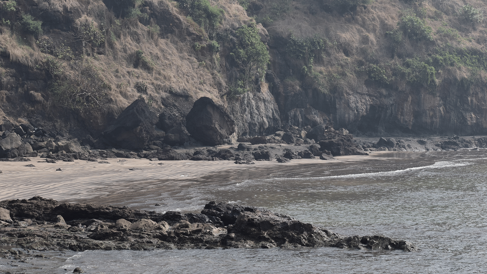 Overview of the alibaugh beach with rocky terrain leading to the sea and mountains in the background