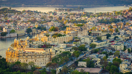 An aerial view of Udaipur nestled along a lake, with mountains in the background.