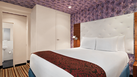 Modern bedroom at Night Hotel Broadway with a neatly made bed, patterned ceiling design, and soft, welcoming lighting.