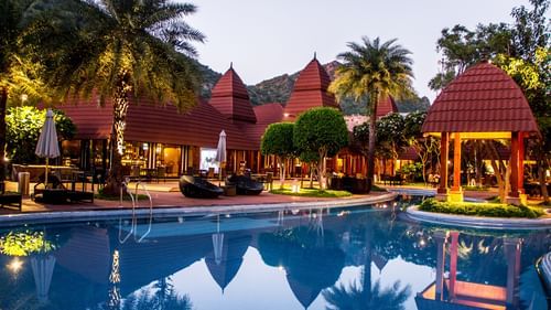 A panorama showing the entire pushkar resort with swimming pool and the cottages under a dusky sky 