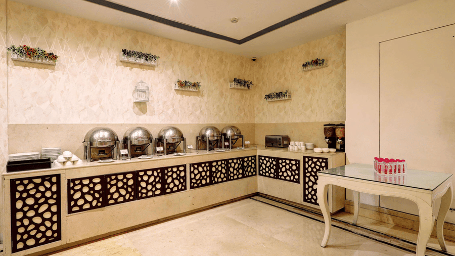 A sleek indoor buffet station featuring polished stainless steel chafing dishes set against a patterned cream wall and decorative lattice woodwork - Flute Boutique By Hotel 91, Jaipur