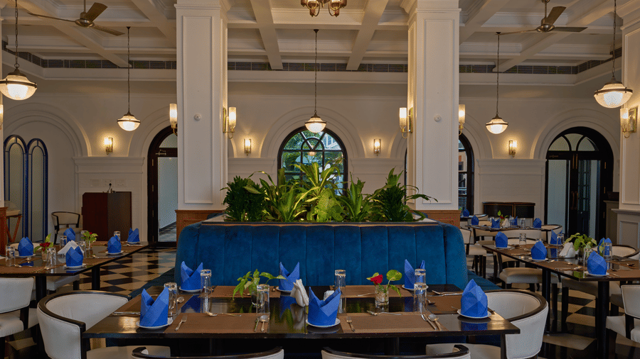 Elegant dining room at the best hotel in Fort Kochi, Old Court House by Abad, featuring a blue velvet booth, white columns, and set tables.