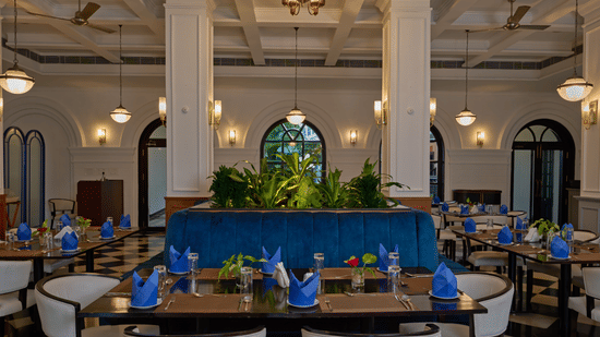 Elegant dining room at the best hotel in Fort Kochi, Old Court House by Abad, featuring a blue velvet booth, white columns, and set tables.