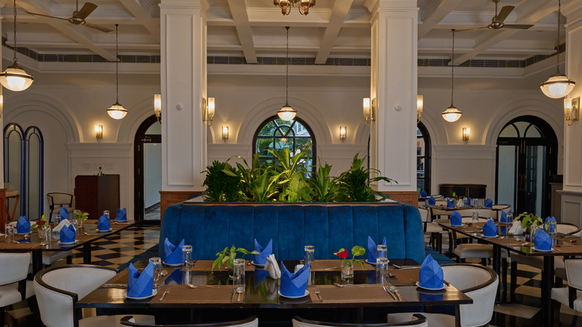 Elegant dining room at the best hotel in Fort Kochi, Old Court House by Abad, featuring a blue velvet booth, white columns, and set tables.