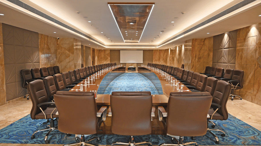 A long oval boardroom table with office rolling chairs rests on a patterned carpet inside the Allure hall at Praveg's Grand Eulogia, Ahmedabad.