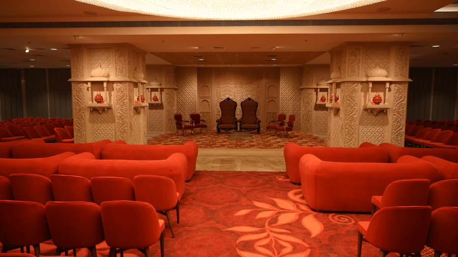 The spacious interiors of Lambic banquet hall featuring comfortable sofa seating and rows of chairs facing a stage area at Praveg's Grand Eulogia, Ahmedabad.
